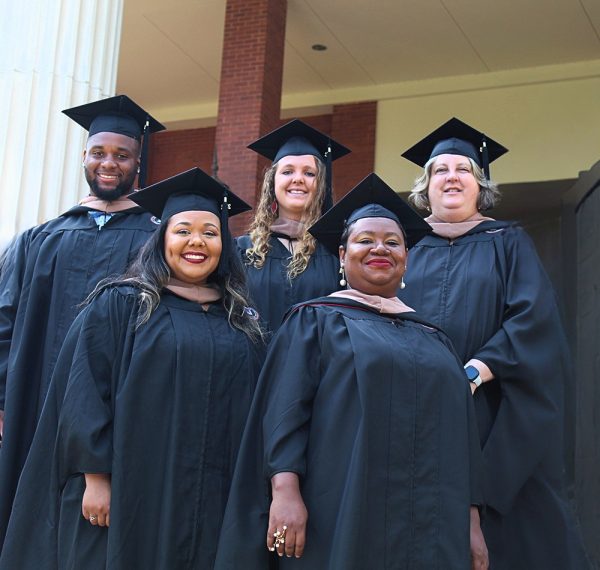 Group of professors standing together smiling for a picture in their cap and gowns for graduation.