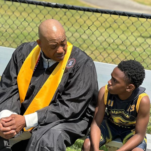 Professor graduation gown and stole sitting on a bench talking to a young teenager wearing a sports uniform.